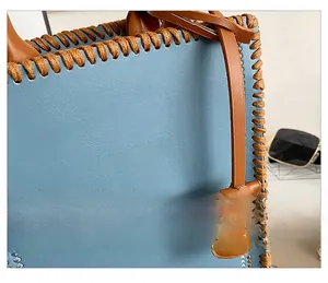 Detail of sky blue pebbled leather tote with brown hand-woven stitching and gold logo