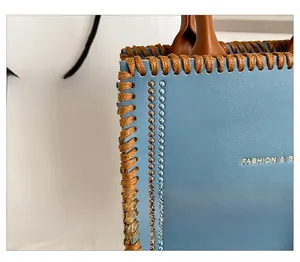 Detailed close-up of blue leather tote bag with brown hand-stitched seams and logo
