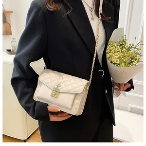 Detail of quilted white crossbody bag with gold chain strap on black blazer