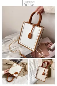 Detailed view of white tote bag with brown leather trim and golden metal chain strap