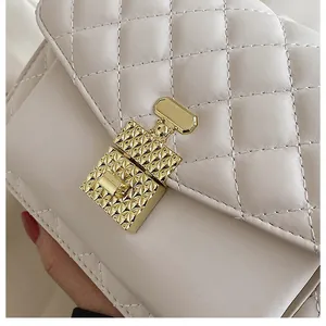 Detail view of the quilted stitching and gold geometric clasp on the beige square bag