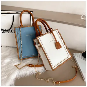 Detail of blue and white two-tone tote bag with woven brown edges and chain strap