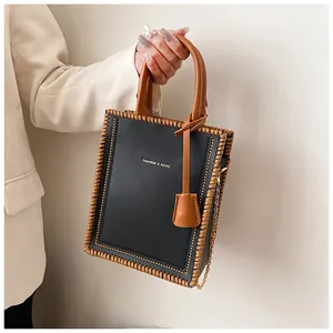 Detail of a black tote bag with brown woven edges and a golden chain strap