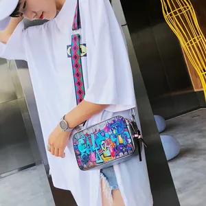Graffiti printed camera crossbody bag with a wide geometric patterned shoulder strap