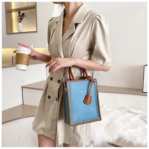 Detail of light blue tote bag with brown woven edges and metal chain shoulder strap