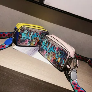 Graffiti camera crossbody bags with colorful wide straps on a wooden surface