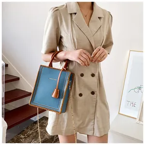 Blue tote bag with brown leather handles and chain strap worn with a beige dress