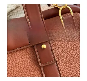 Détail d'un sac en cuir grainé avec coutures précises et rivets métalliques dorés