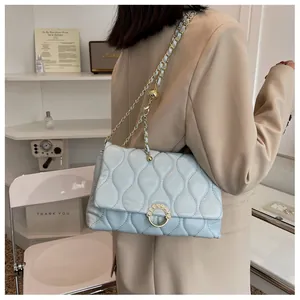 Détail d'un sac matelassé bleu clair avec chaîne dorée et boucle perle sur un blazer
