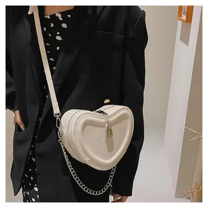 Detail of white heart-shaped crossbody bag with metal lock and chain strap on model