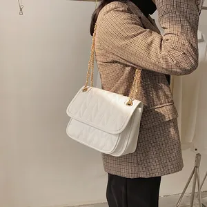 White quilted crossbody bag with gold chain strap shown on model in a brown blazer