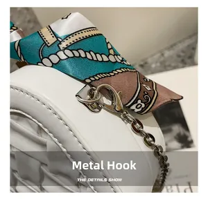 Detail showing the silver metal hook, chain strap and silk scarf on a white leather handbag