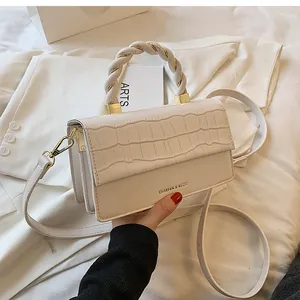 Detailed close-up of cream-colored crossbody bag with crocodile texture and twisted handle