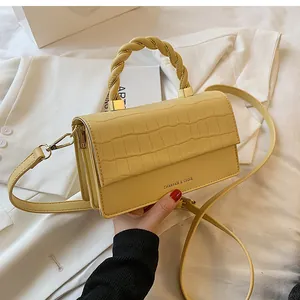 Detail of cream yellow square bag with crocodile pattern and braided handle