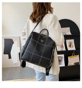 Détail d'un sac à dos en cuir noir avec surpiqûres blanches porté par un mannequin
