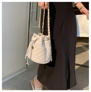 Witte gewatteerde bucket bag met gouden ketting en trekkoord gedragen met een zwarte jurk