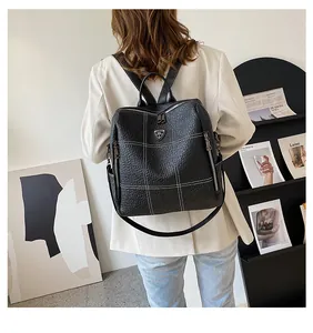 Détail d'un sac à dos en cuir grainé noir avec surpiqûres blanches et logo bouclier en métal