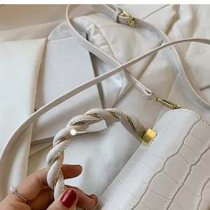 Close-up of white crocodile pattern handbag with twisted handle and gold hardware