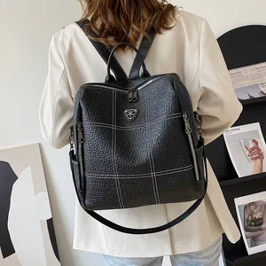 Sac à dos en cuir noir avec surpiqûres blanches et logo en métal porté par un mannequin