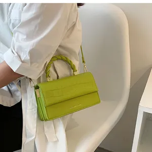 Detail of neon green crocodile texture handbag with twisted handle on white shirt