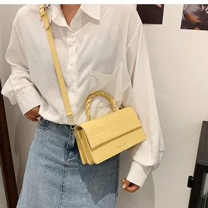 Detail of yellow crocodile embossed handbag with twisted handle and branding on model