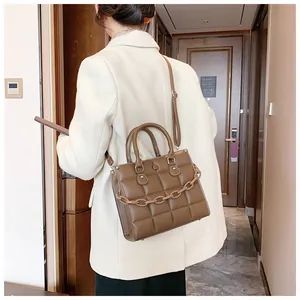Detail view of a brown quilted square bag with chunky chain strap worn crossbody style