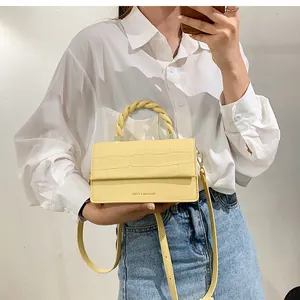 Detail of light yellow crocodile-textured crossbody bag with woven handle and logo
