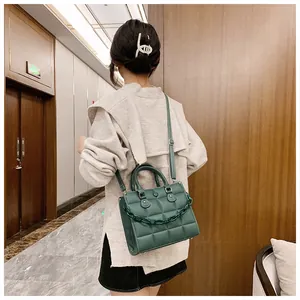 Detail of dark green quilted mini handbag featuring acrylic chain and leather strap