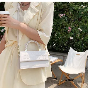 Detail of cream white crossbody bag featuring crocodile pattern and woven handle