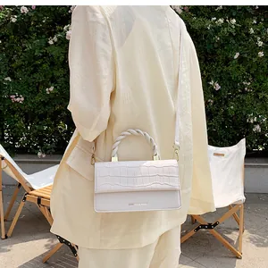 Detail of white crocodile embossed handbag with woven handle and adjustable strap