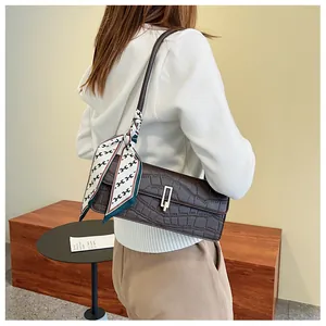 Dettaglio borsa baguette marrone scuro con trama a coccodrillo e foulard di seta alla moda
