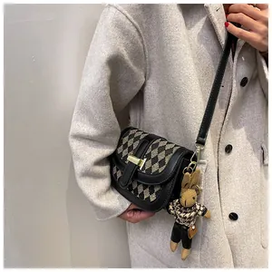 Detalle de un bolso de silla de montar a cuadros con diseño acolchado y dije de conejo