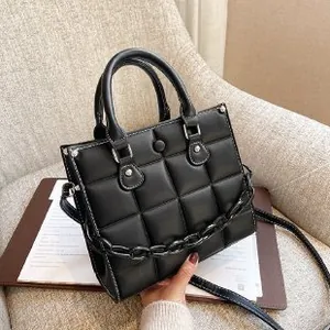 Minimalist black quilted PU leather crossbody bag with chain and top handles on a chair