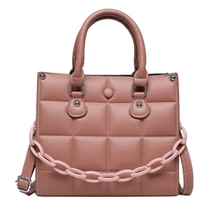 Pink quilted square handbag with resin chain and adjustable leather strap on white background
