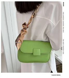 Detail of green leather shoulder bag featuring silk scarf chain strap and golden buckle