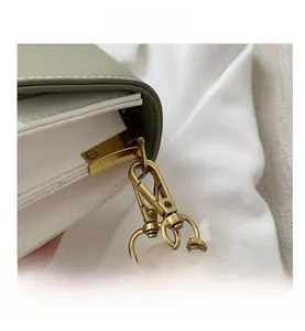 Close-up of retro gold metal chain hook on a minimalist green and white leather crossbody bag
