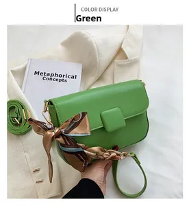 Close-up of green leather shoulder bag with decorative silk scarf on a white blazer