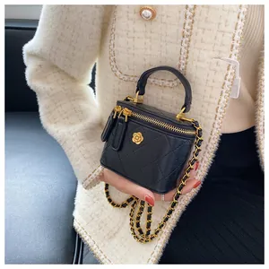 Detail of black quilted mini box bag with gold flower emblem and chain strap
