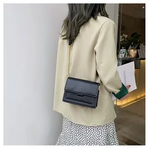 Detail view of the black leather crossbody bag with white stitching and gold chain strap