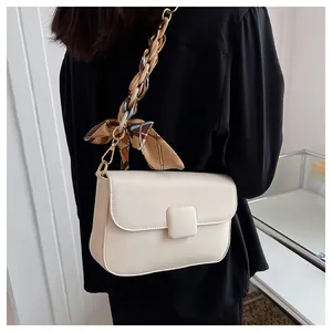 Detail of off-white crossbody bag featuring silk scarf wrapped metal chain strap