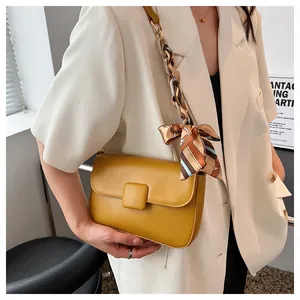 Close-up of yellow leather shoulder bag with decorative silk scarf on chain strap