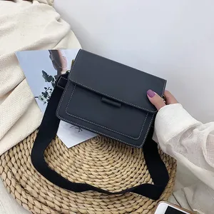 Minimalist black square crossbody bag with white contrast stitching and wide fabric strap