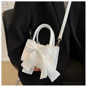 Close-up of white mini handbag featuring a large bow detail and gold hardware on model