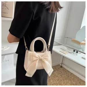 Detail of a chic beige crossbody bag with a large bow and gold metal strap hooks