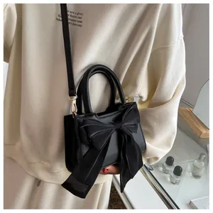 Detail of elegant black crossbody bag with large satin bow and adjustable strap