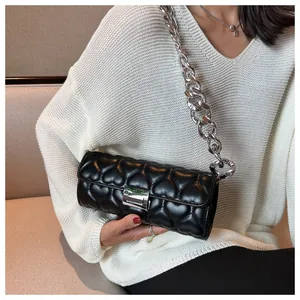 Détail du sac cylindre noir à surpiqûres cœur avec chaîne argentée porté par un mannequin