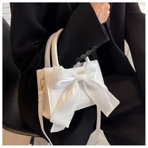 Detailed view of a white leather handbag with a large satin bow and sleek handle