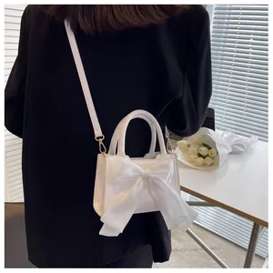 Detail view of white leather crossbody bag with a large organza bow and golden hardware