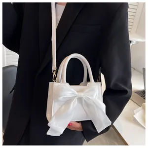 Detail of white leather crossbody bag with oversized organza bow on black blazer