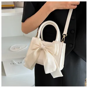 Chic beige square handbag with large mesh bow detail worn by model in black outfit